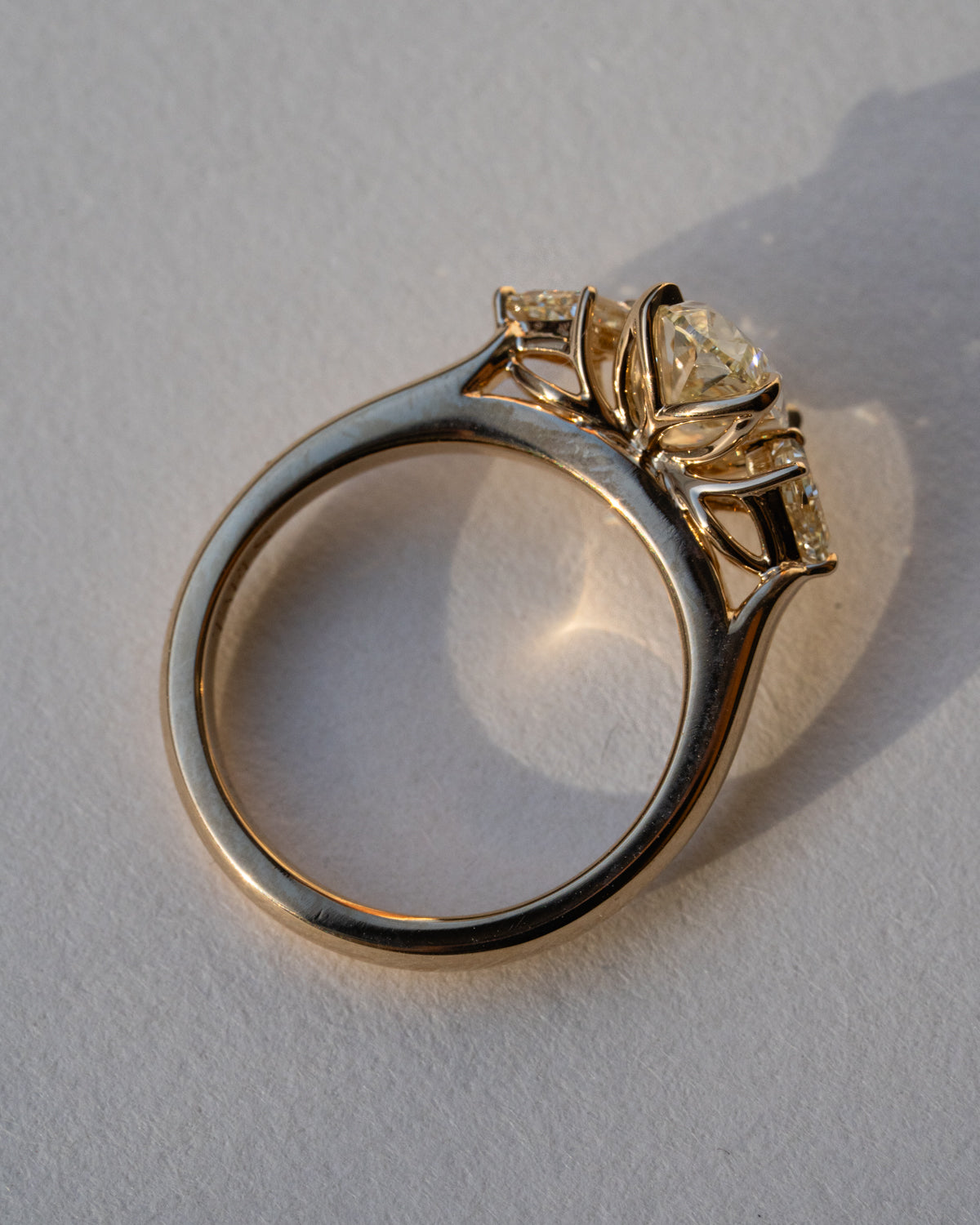 Side profile of oval diamond three-stone ring in 18k yellow gold showing setting depth and band profile