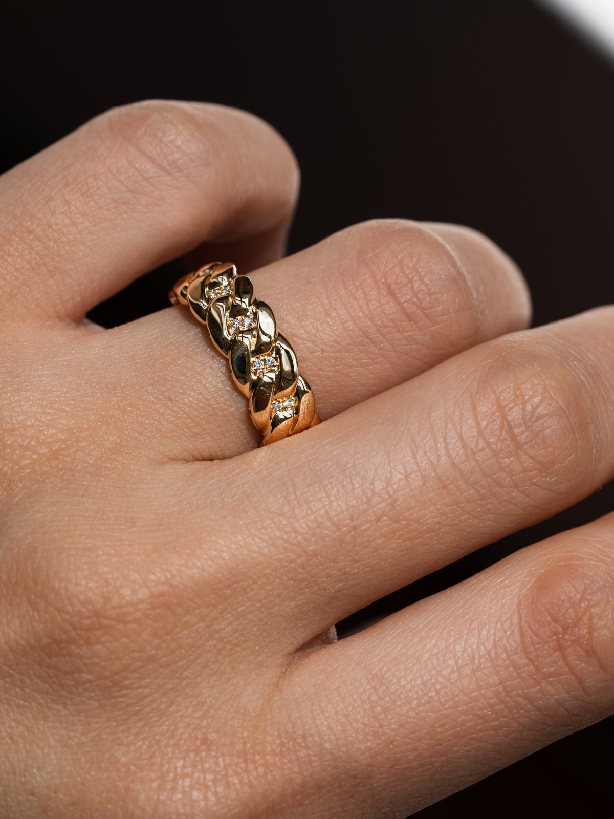 Gold ring on a finger against a dark background Side profile view of custom Cuban link chain engagement ring showing diamond pavé detail and sculptural yellow gold links