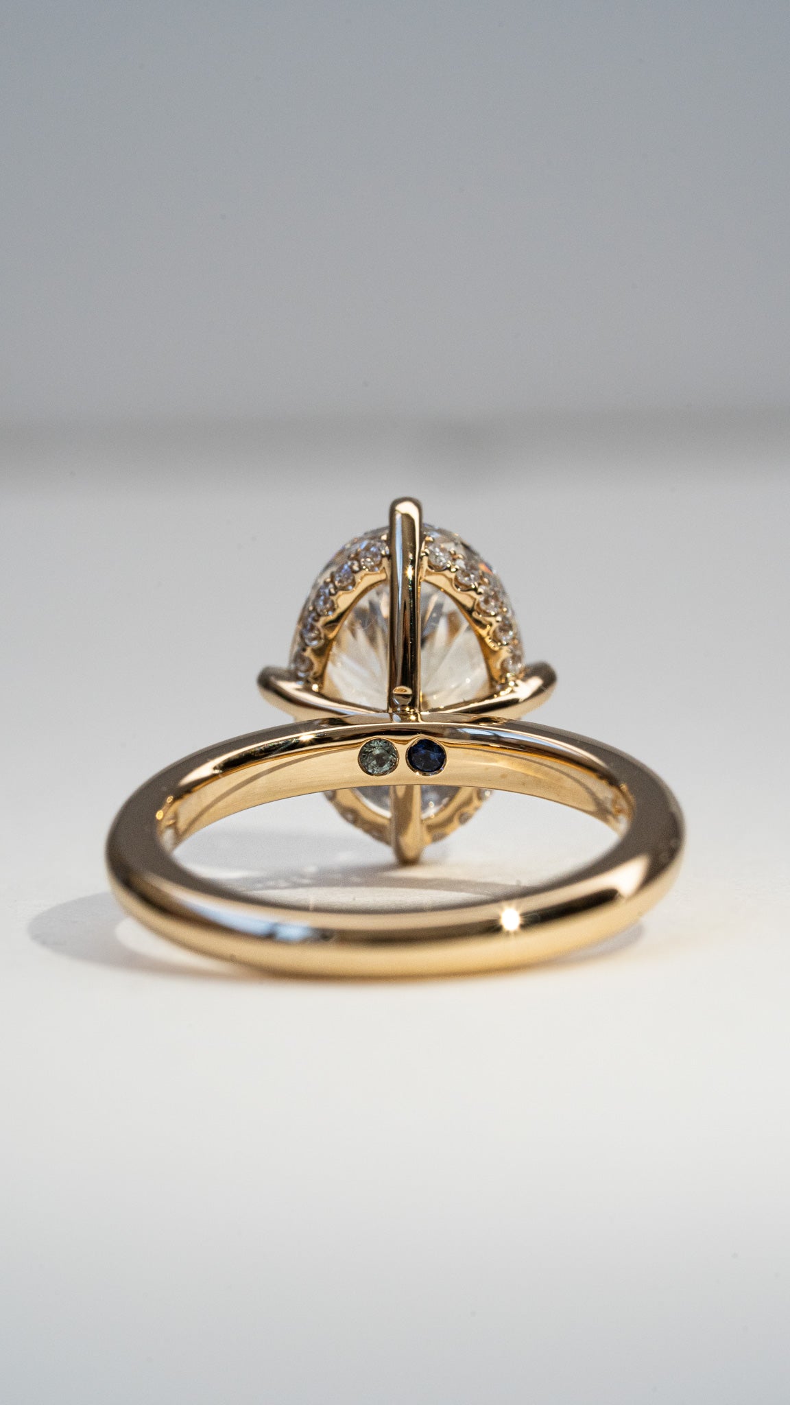 A gold ring with a large oval clear gemstone pavé-set on top of a polished gold band, photographed on a neutral light gray background.