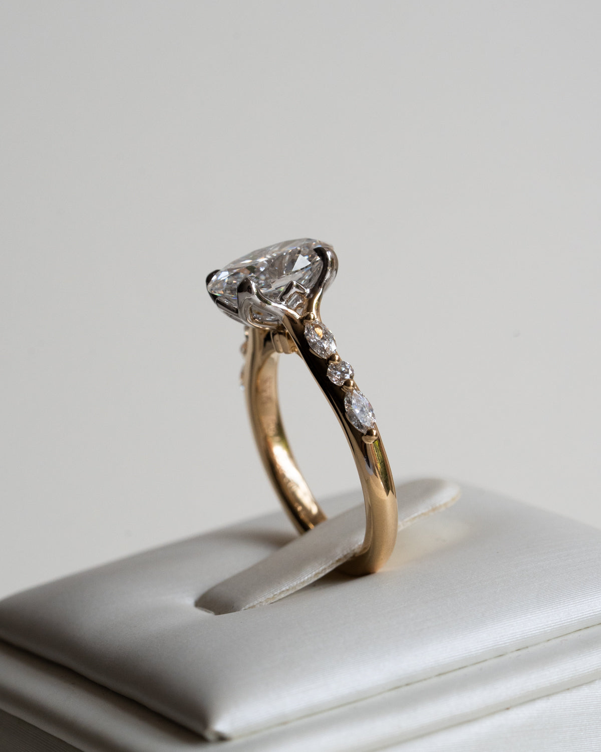 Oval diamond engagement ring on hand with marquise and round diamond shoulder details