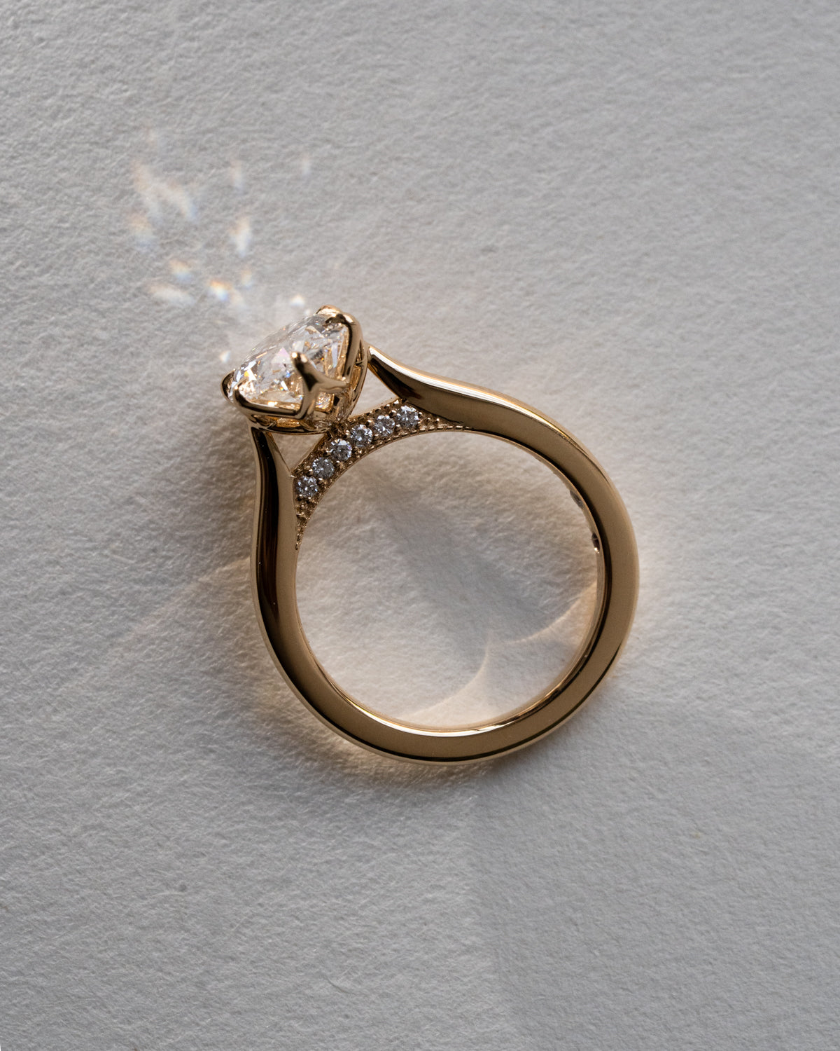 Custom oval cut diamond engagement ring with overlapping floral prongs in yellow gold, side view showing pavé set bridge and unique sculptural setting