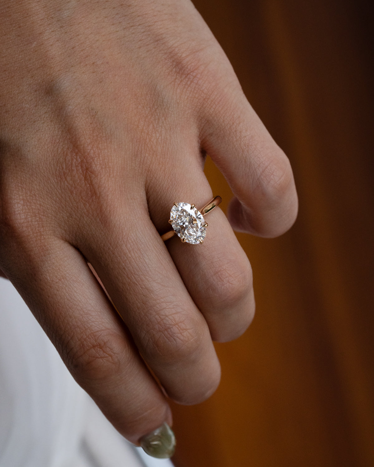 Custom oval cut diamond engagement ring with overlapping floral prongs in yellow gold, side view showing pavé set bridge and unique sculptural setting on hand