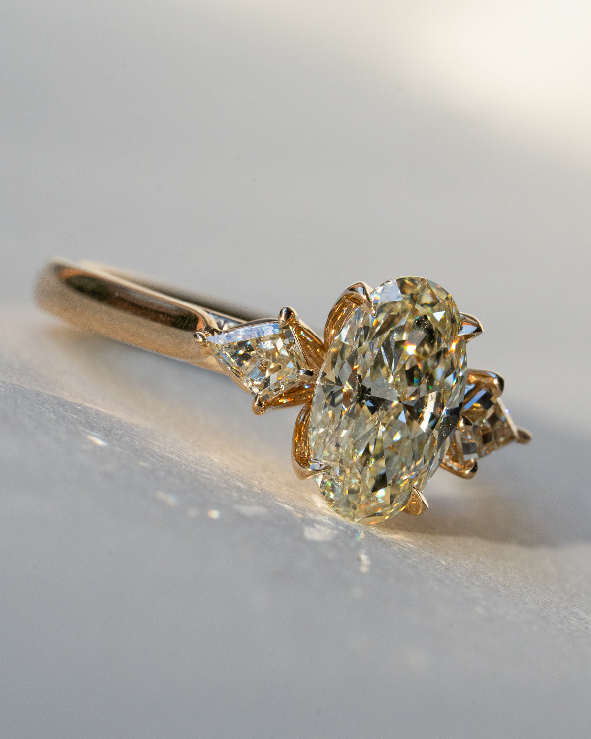 Three-stone oval diamond ring with kite sides in yellow gold, wider front view on surface