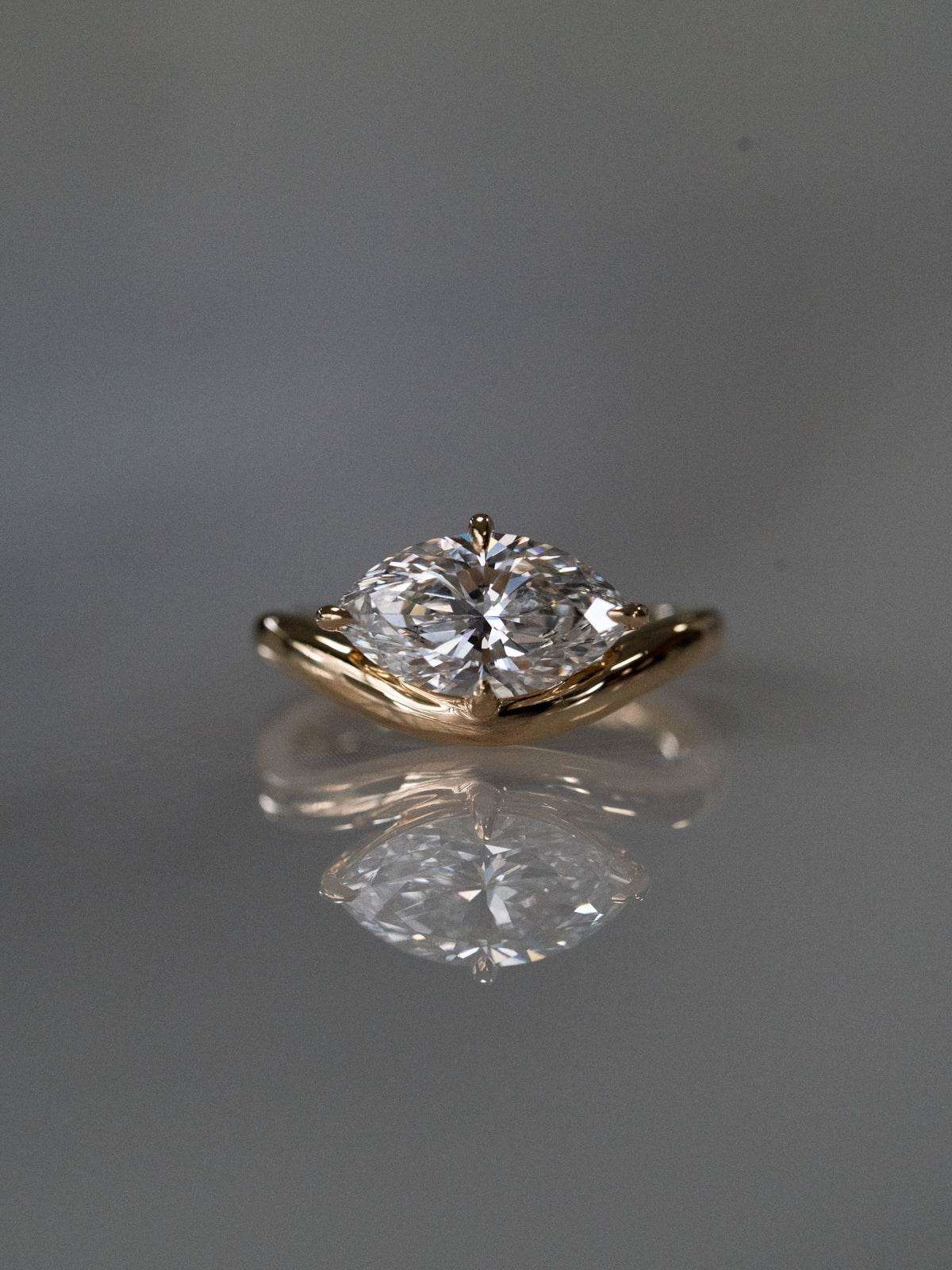 Gold ring with a marquise diamond on a reflective gray surface in 18ct yellow gold. 