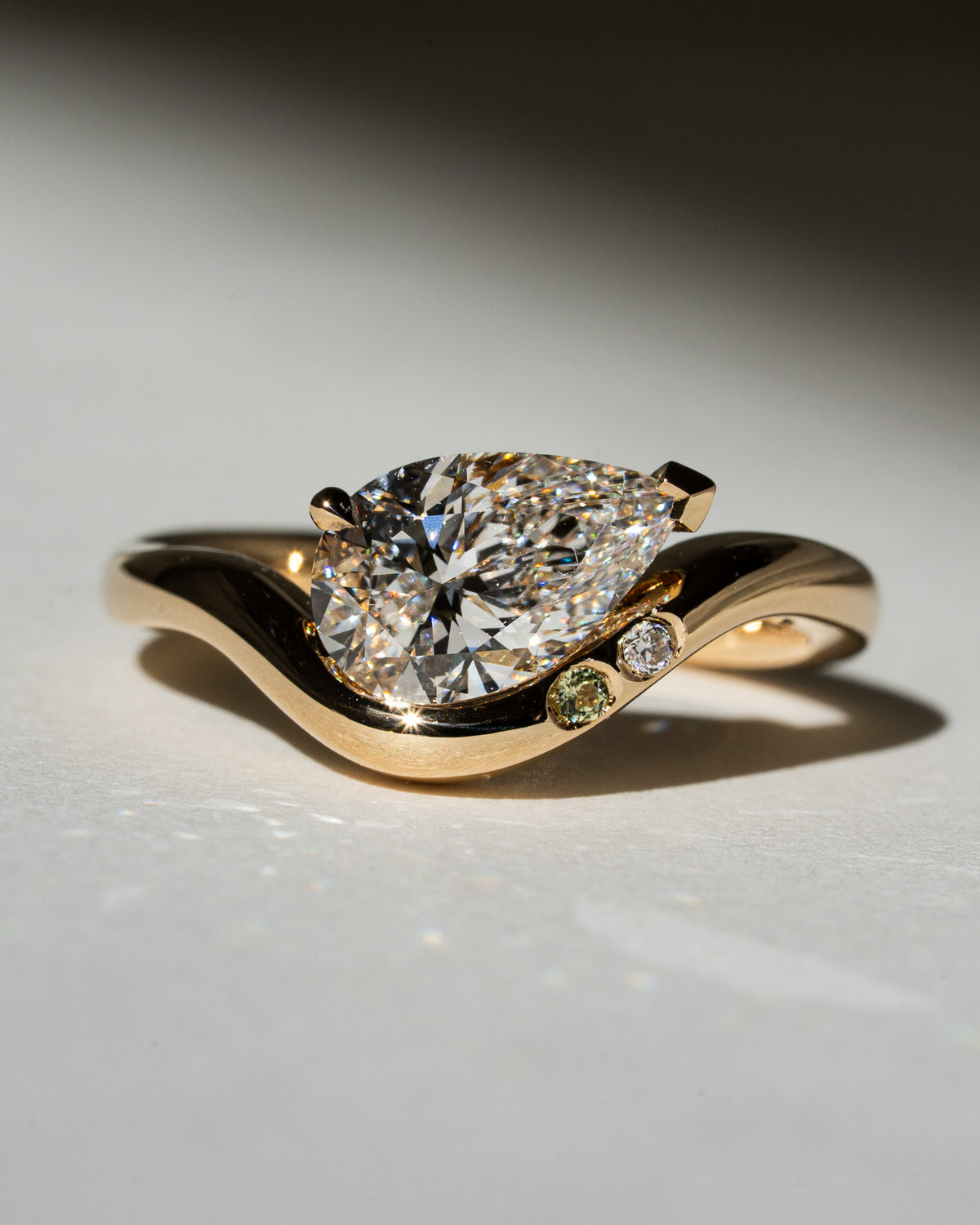 Pear diamond on curved band with personal birthstones on the band set in v-tip and claw prong and bezel setting