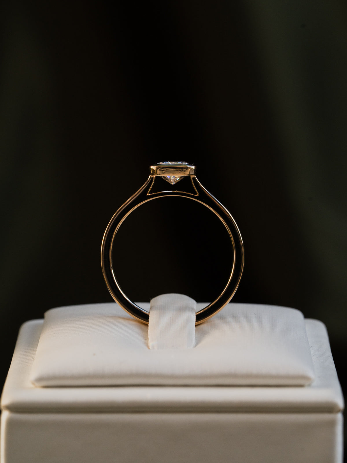 Gold bezel floating cathedral ring on a white stand with a dark background